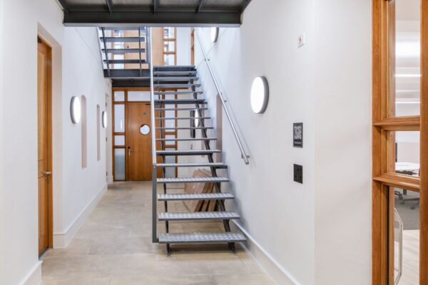 A modern interior stairwell with metal stairs and wooden doors at 45 Broadwick Street, London.