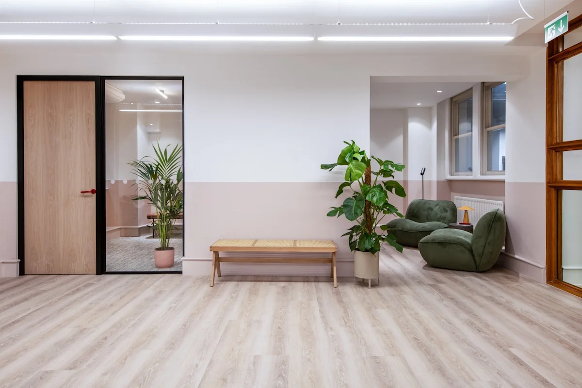 A modern office interior at Broadwick Street 45, London, featuring plants, a wooden bench, and green lounge chairs.