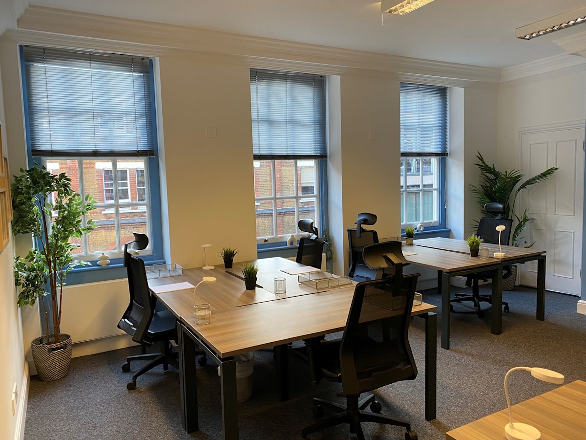 A modern office space with several desks, chairs, plants, and large windows on Broadwick Street in London.