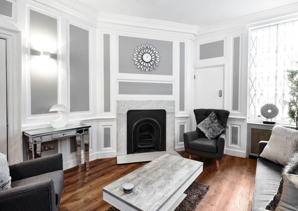 A stylish living room with modern gray and white decor featuring a clock above a fireplace.