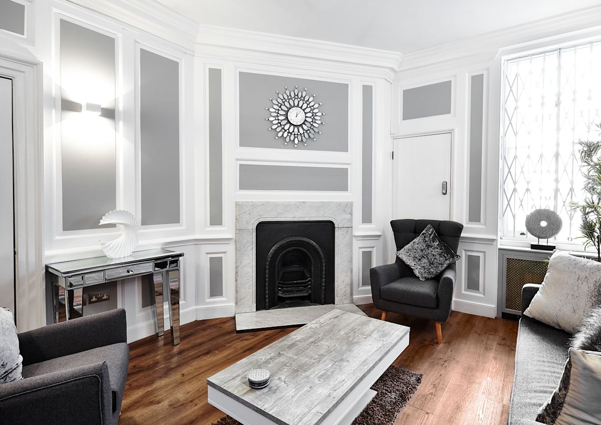 A stylish living room with modern gray and white decor featuring a clock above a fireplace.