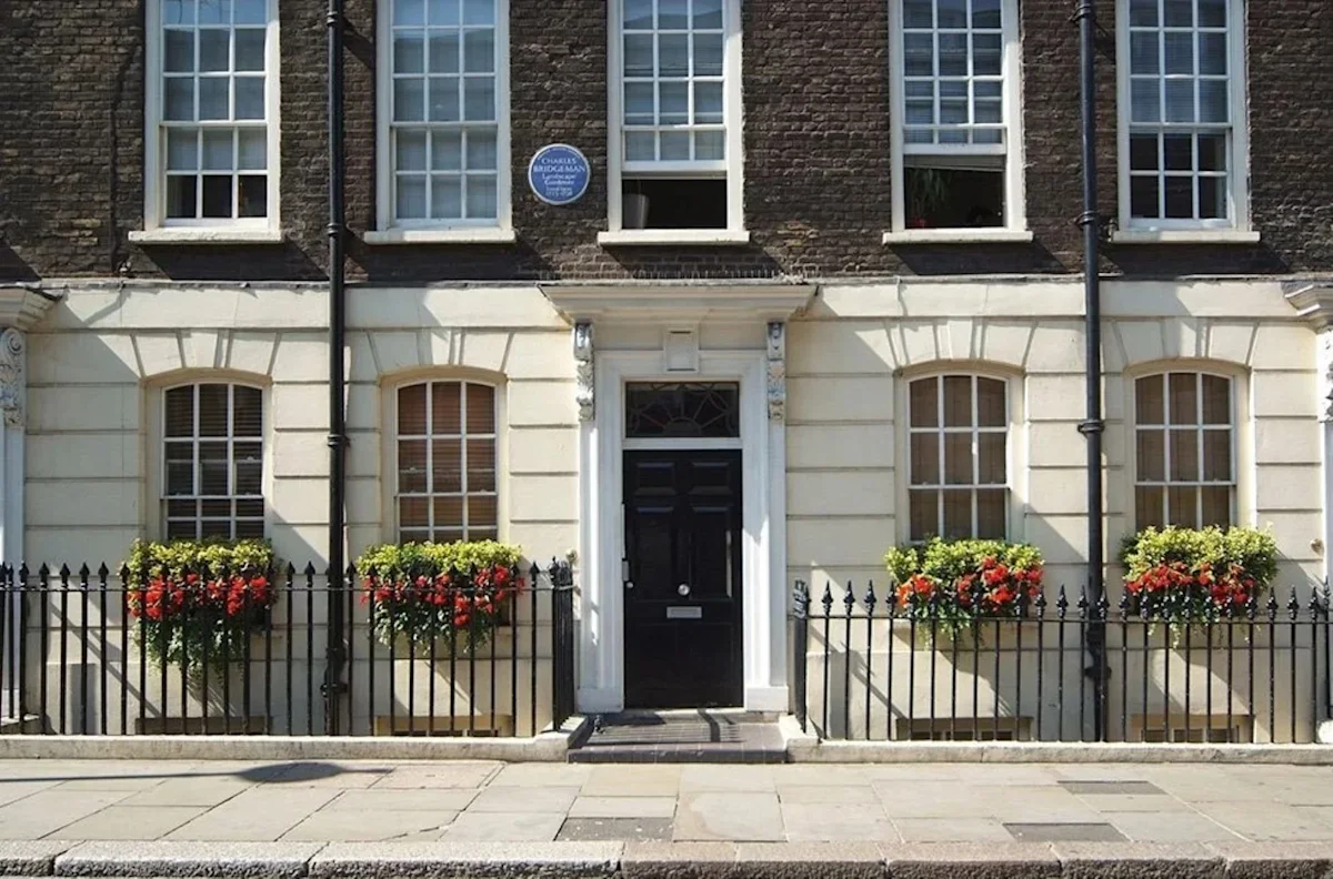 Facade of a historic building on Broadwick Street with flower boxes and a blue plaque.
