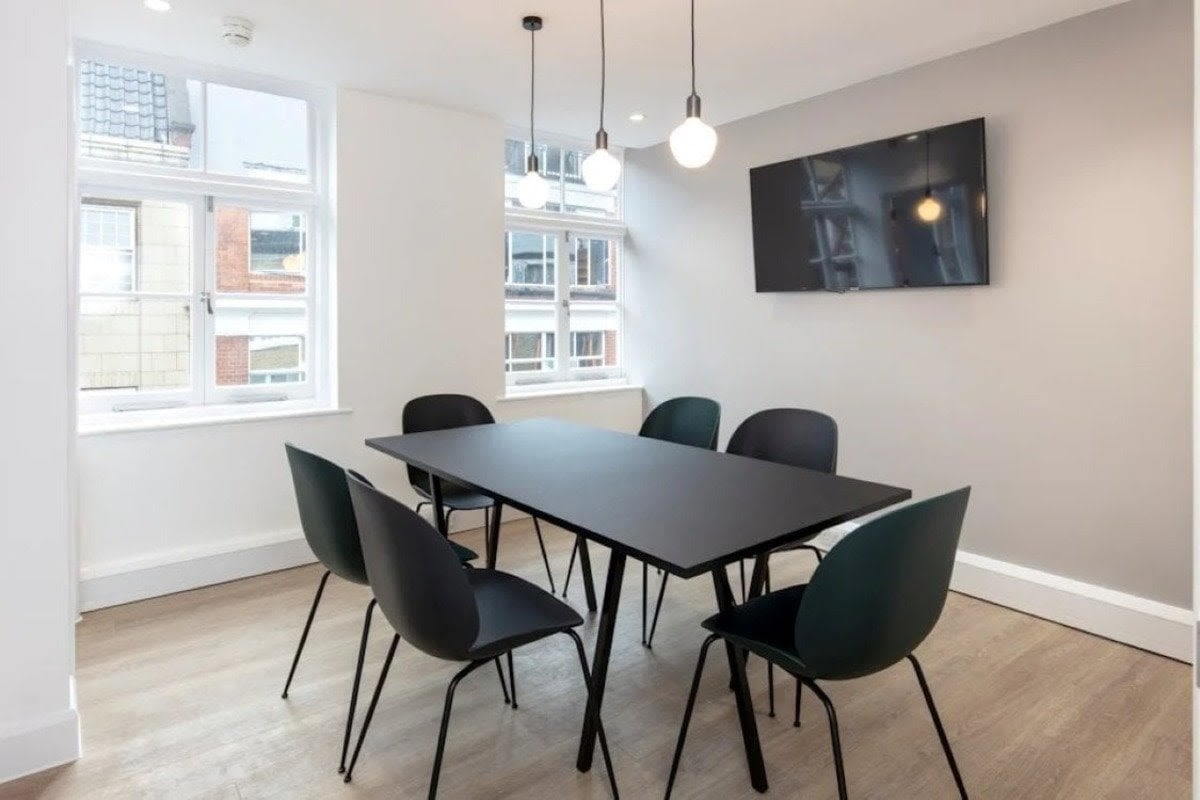 A modern meeting room with a black table, six chairs, hanging lights, and a wall-mounted TV.