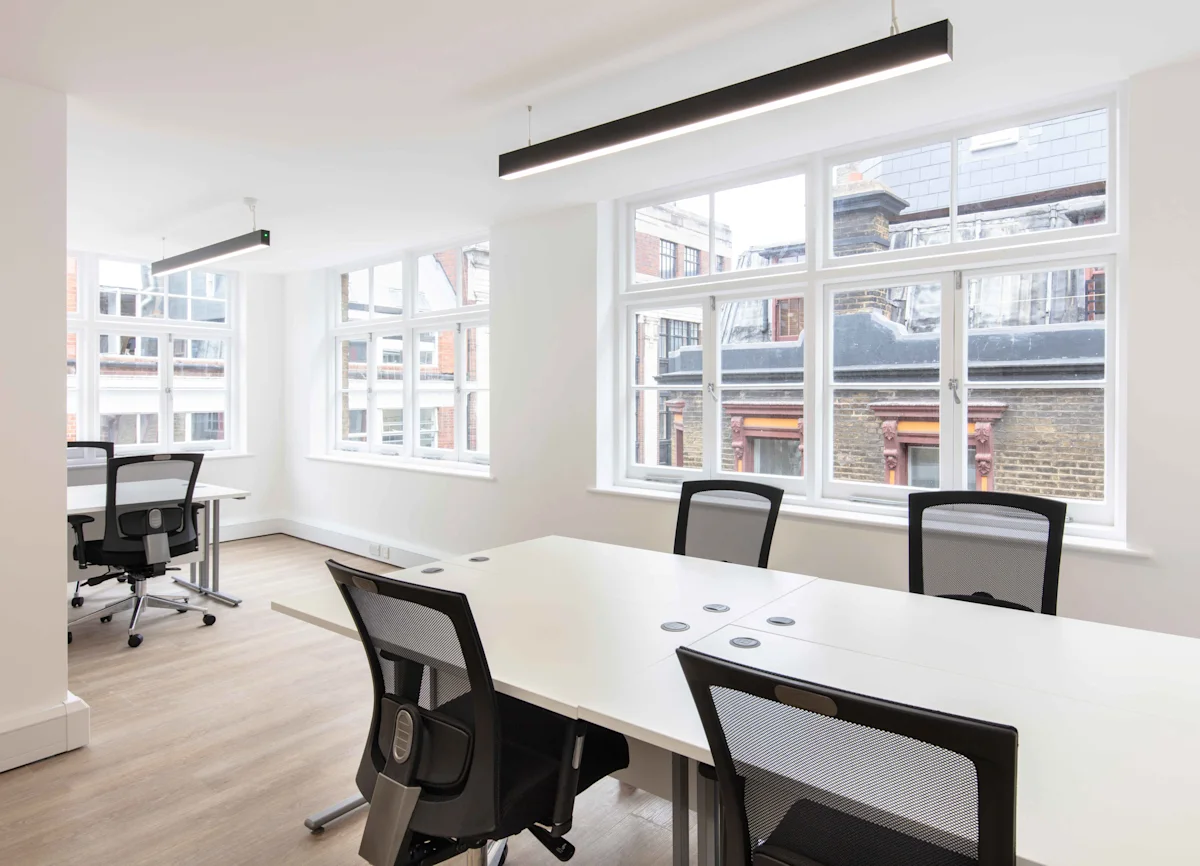 A bright, modern office space with large windows, white desks, and black office chairs at Broadwick Street, London.
