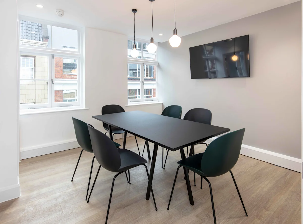 A modern meeting room with a black table, six chairs, hanging lights, and a wall-mounted TV.
