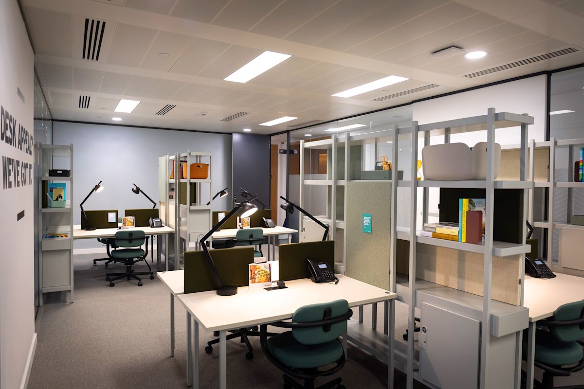 Modern open-plan office space with multiple workstations and shelving units.