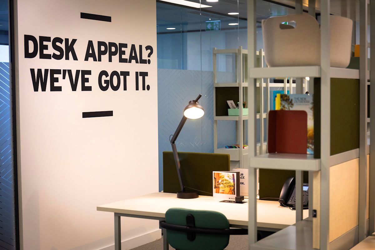 A modern office desk at Cabot Square 25 in London with a motivational wall message.