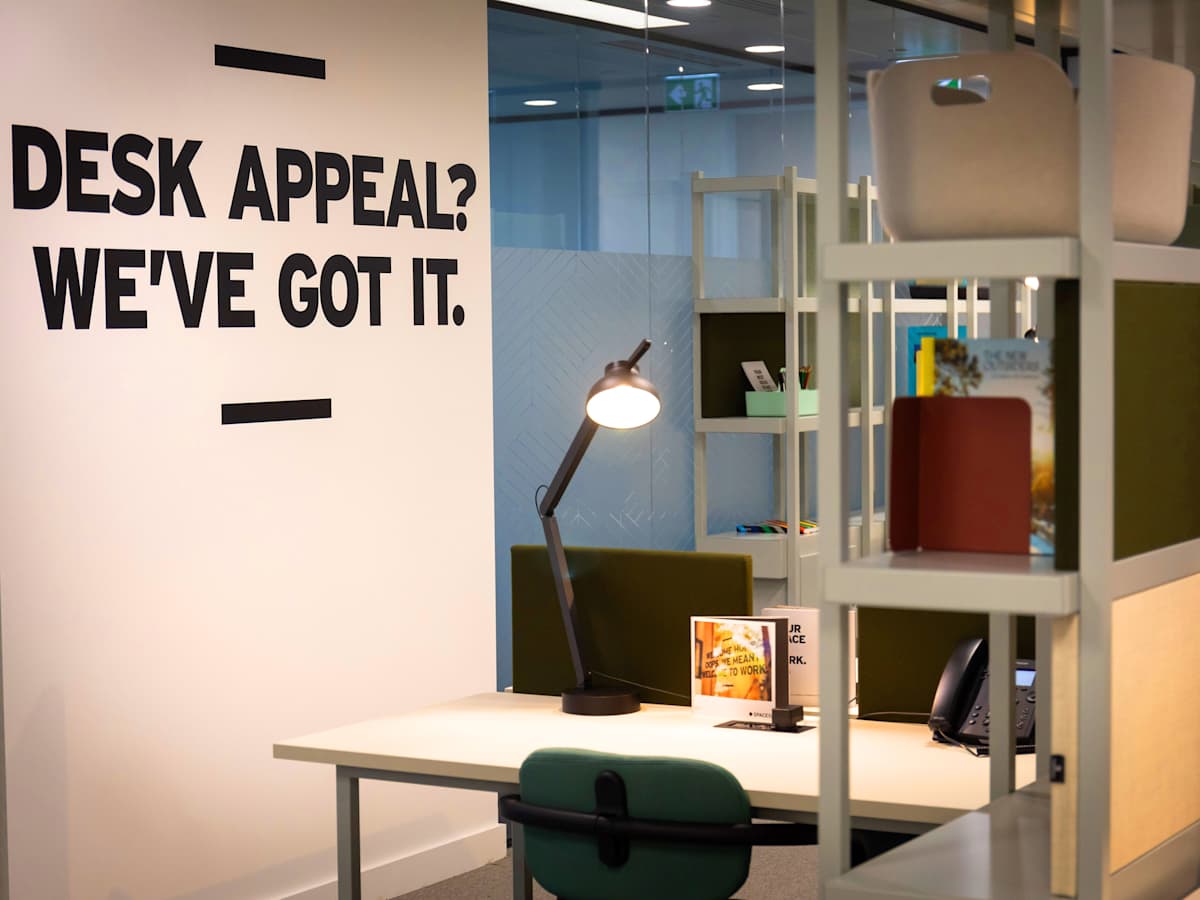 Modern office space at Cabot Square 25, London, featuring a stylish desk setup with a motivational wall quote.
