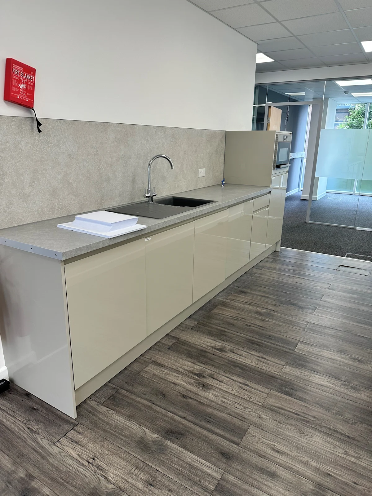 Modern office kitchenette with a sleek design and wood flooring.