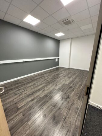 An empty office room with wooden flooring and grey walls, located on the ground floor of Cadmus Court in London.