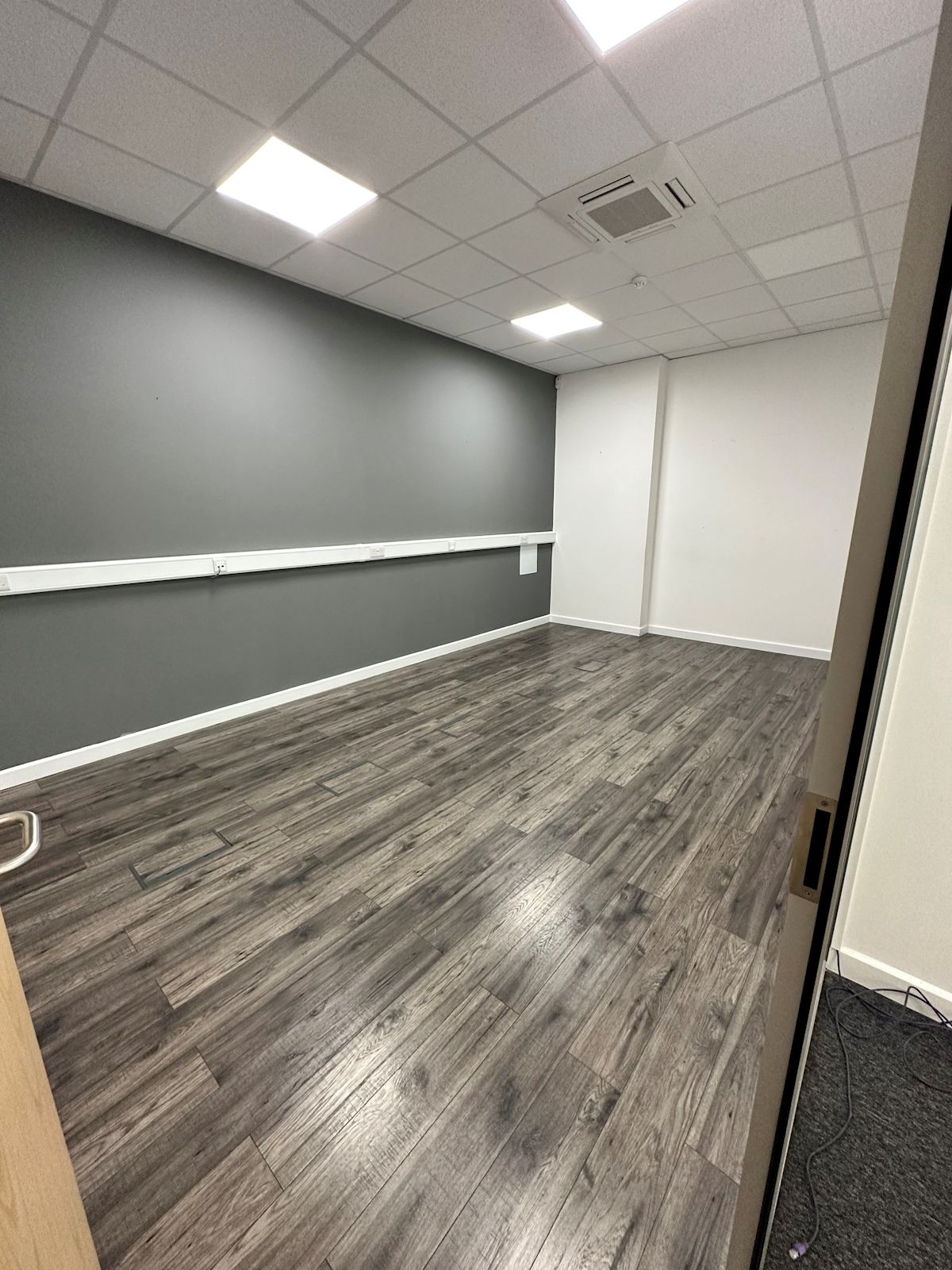 An empty office room with wooden flooring and grey walls, located on the ground floor of Cadmus Court in London.