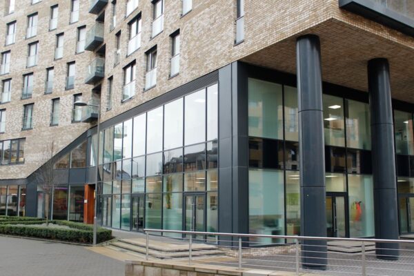 Modern ground floor exterior of Cadmus Court in London with large glass windows and tall black columns.