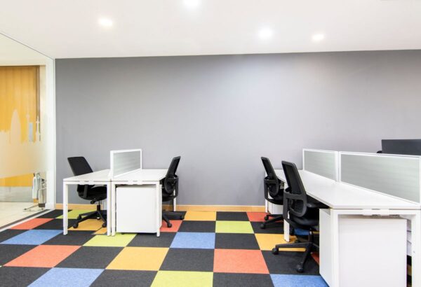 A modern office interior with white desks, black chairs, and a colorful checkered carpet.