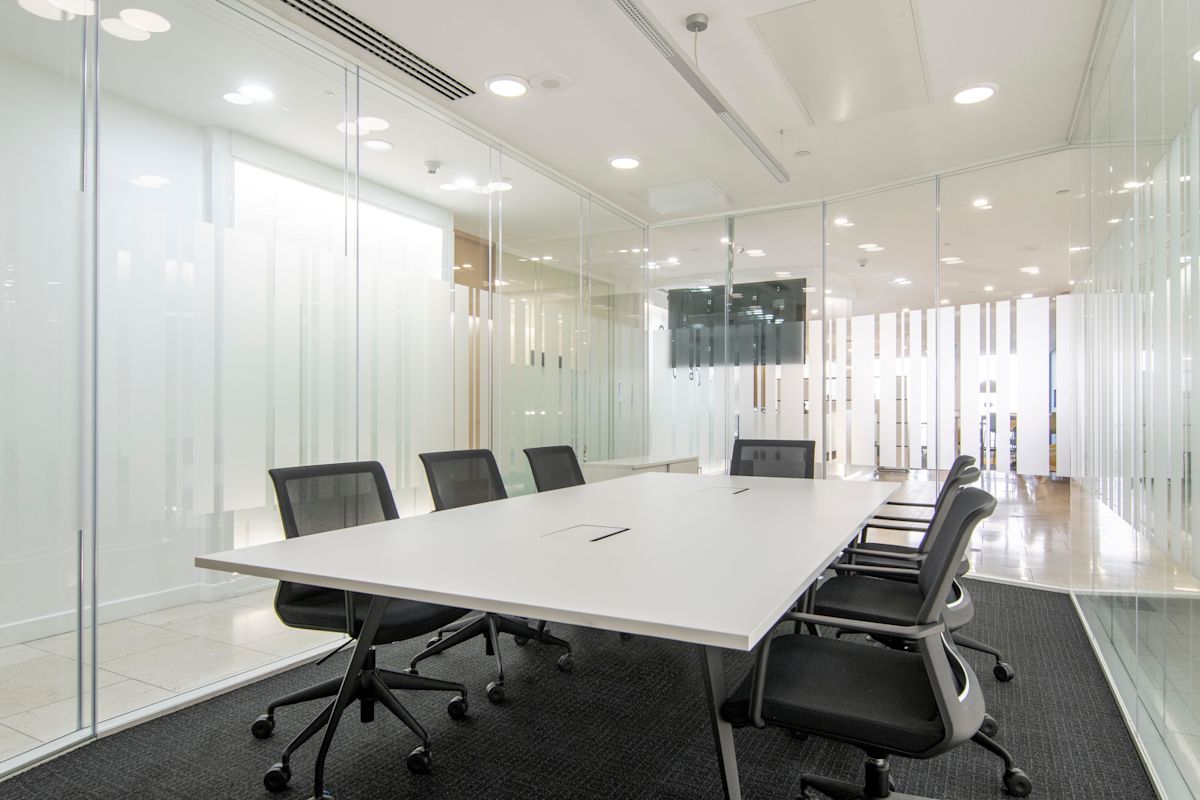 A modern conference room in Canada Square 1, London, with a long table, office chairs, and glass walls.