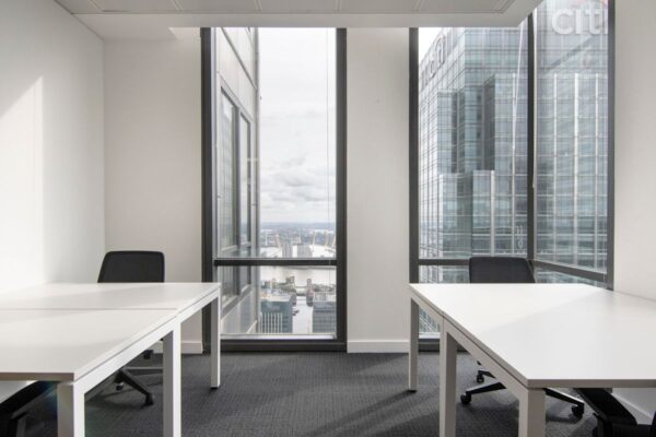 An office room with white desks and chairs, featuring a view of Canada Square in London through large windows.
