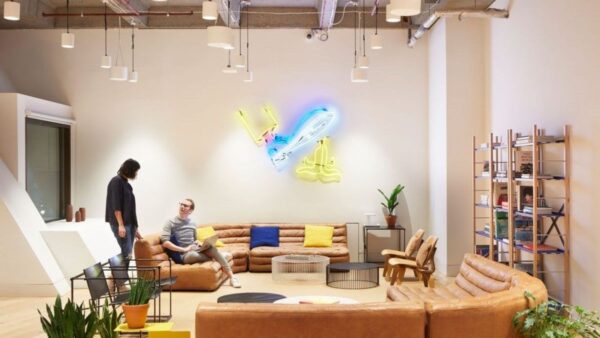 A modern office lounge featuring leather sofas, colorful cushions, and a neon wall art installation.