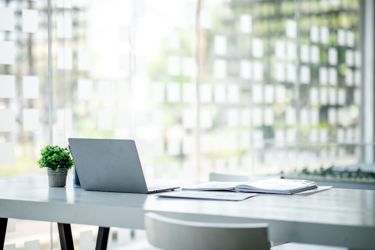 A modern office workspace with a laptop, open book, and small plant on a table.