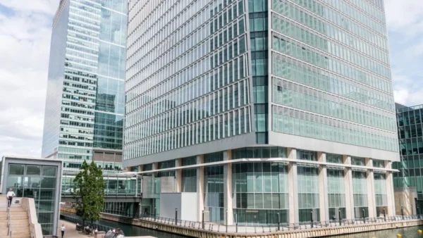 The image shows the modern glass facade of Churchill Place 30 in London, adjacent to a canal.