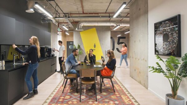 A modern office break area with people relaxing and using a kitchenette.