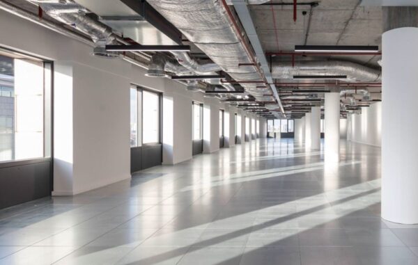 A spacious, empty office space with large windows and exposed ductwork in Clove Crescent, London.