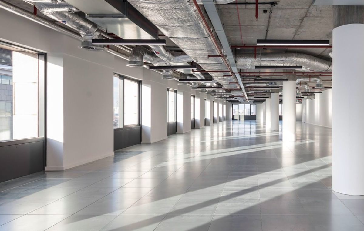 A spacious, empty office space with large windows and exposed ductwork in Clove Crescent, London.