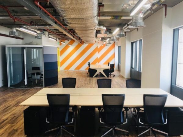 Modern office space at Clove Crescent 2, featuring open desks, a private meeting pod, and a vibrant orange and white striped wall.