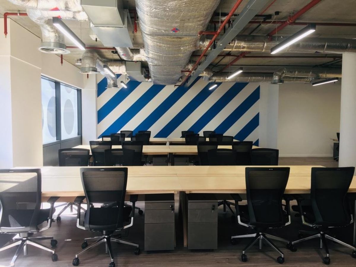 A modern office space in Clove Crescent, London, featuring desks with chairs and exposed ceiling ductwork.