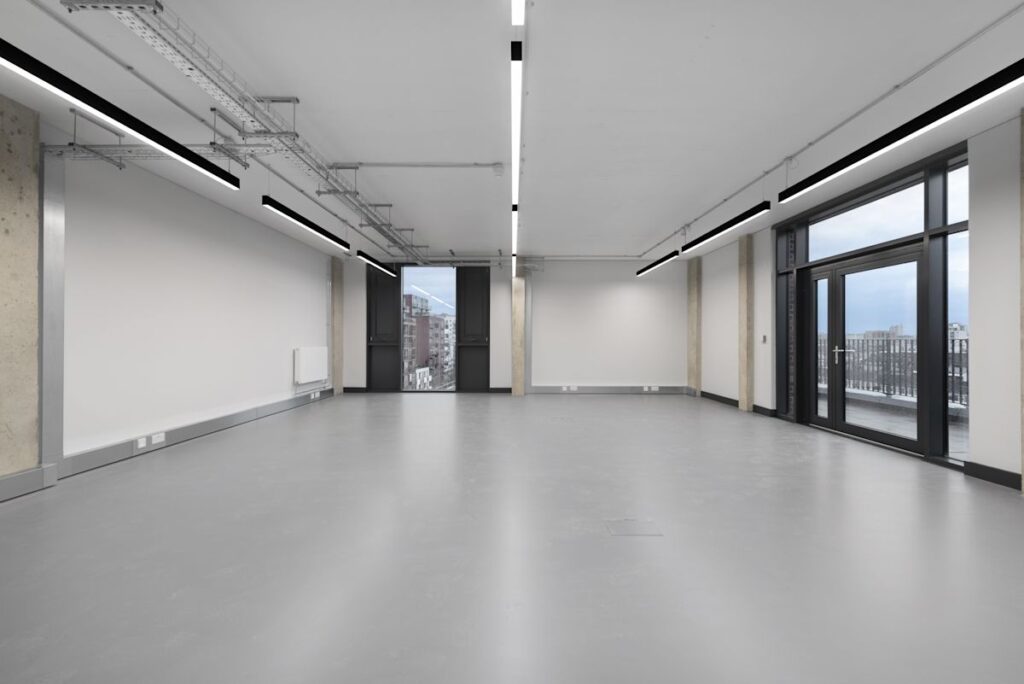 The image shows a spacious, modern empty office interior with large windows overlooking London.