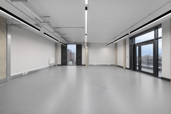 The image shows a spacious, modern empty office interior with large windows overlooking London.