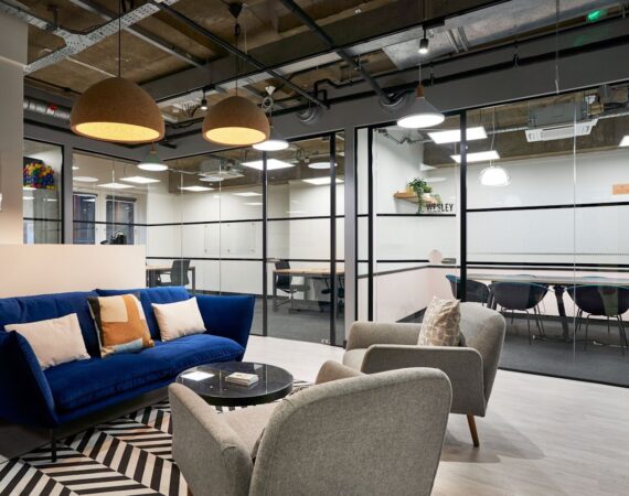 Modern office lounge area with blue sofa, gray chairs, and glass-walled meeting rooms at Crown Place 4, London.