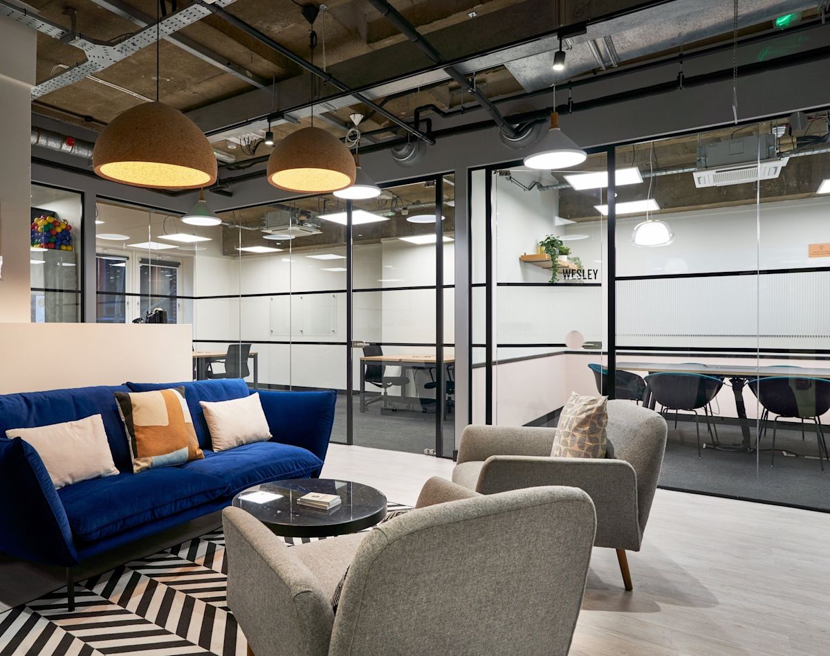 Modern office lounge area with blue sofa, gray chairs, and glass-walled meeting rooms at Crown Place 4, London.