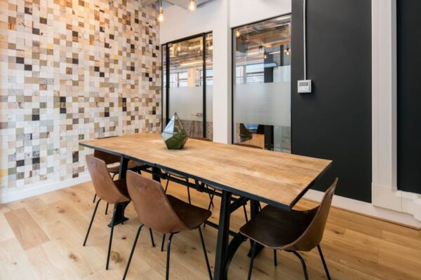 Modern office meeting room with a wooden table, leather chairs, and a tiled accent wall.