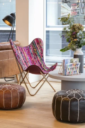 A cozy seating area with a colorful chair, poufs, and a table with a vase of flowers.