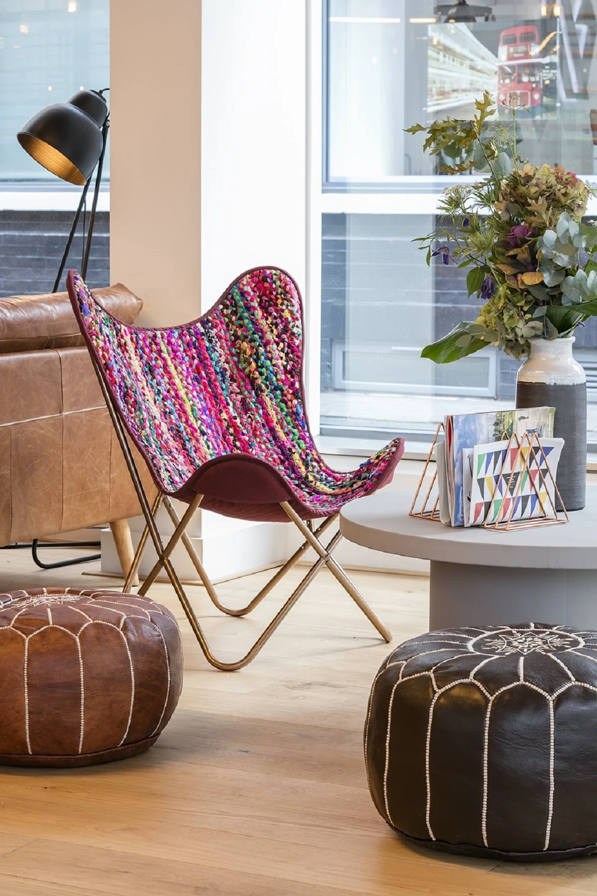 A cozy seating area with a colorful chair, poufs, and a table with a vase of flowers.