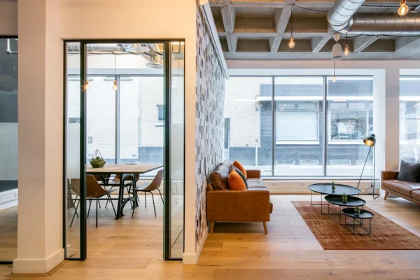 A modern office interior with glass partitions, cozy seating area, and large windows.