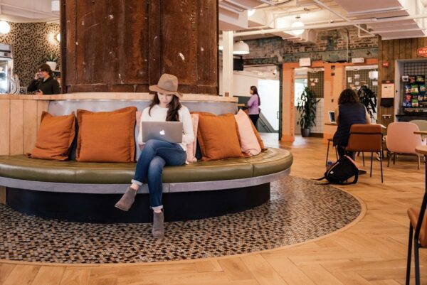 A woman sitting on a circular bench in a stylish co-working space with a laptop.