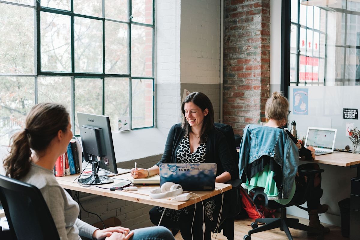 Three people working and chatting in a bright, modern office space.