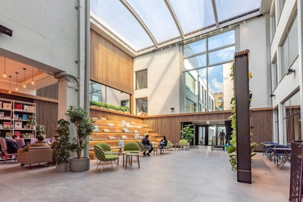 A modern, glass-roofed atrium with seating, greenery, and bookshelves at Folgate Street 35-41 in London.