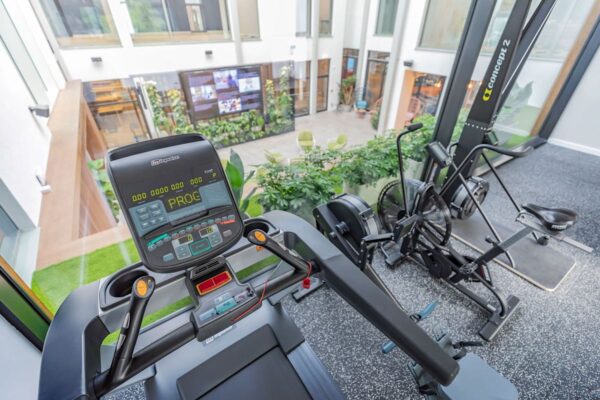 View of a gym with exercise equipment overlooking a green courtyard.
