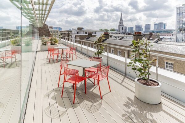 A rooftop terrace on Folgate Street, London, featuring red chairs and tables with a cityscape view in the background.