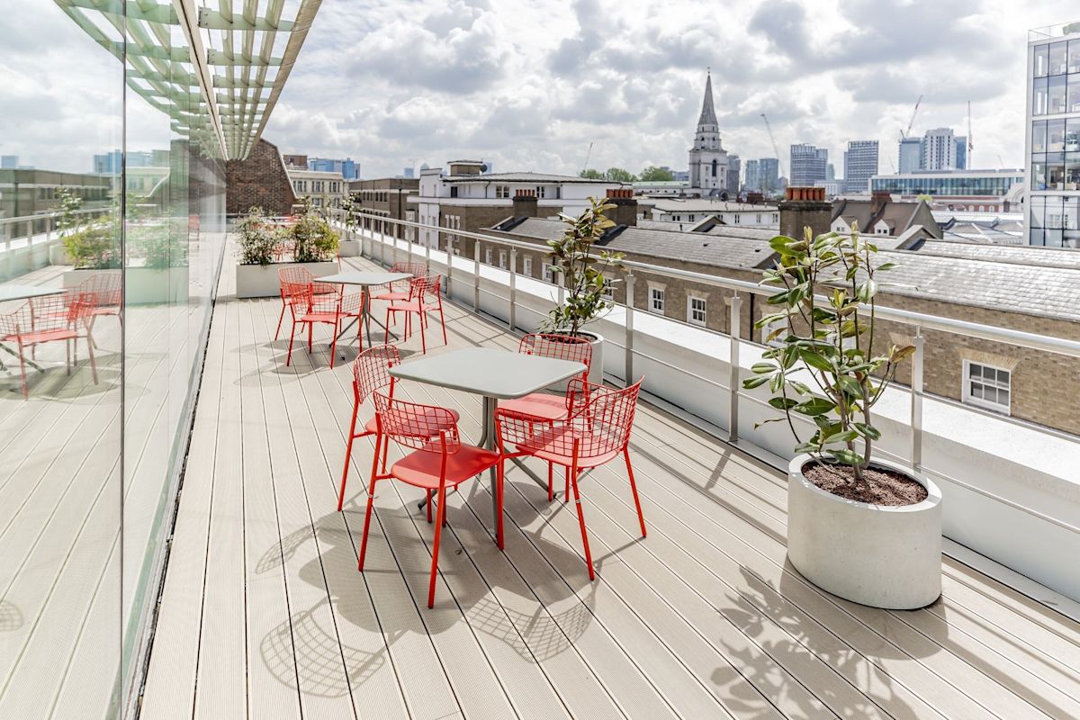 A rooftop terrace on Folgate Street, London, featuring red chairs and tables with a cityscape view in the background.