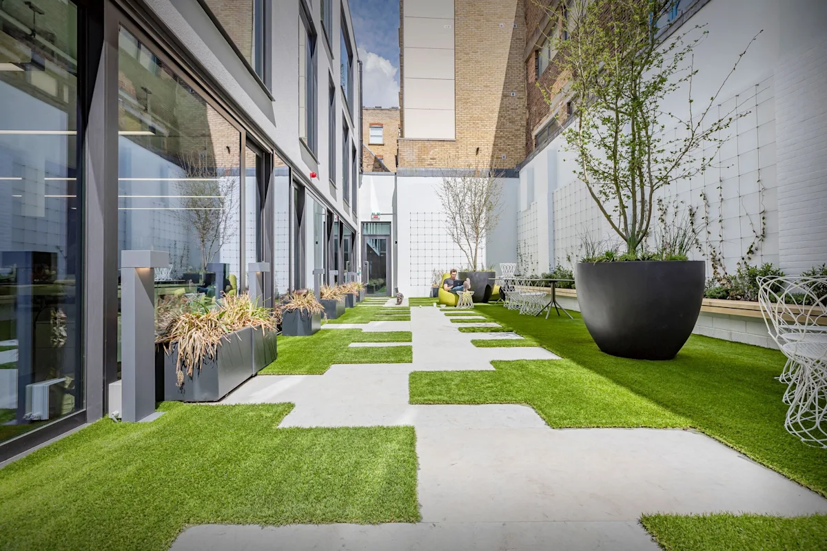 Modern courtyard with green artificial grass and large planters at Folgate Street 35-41, London.