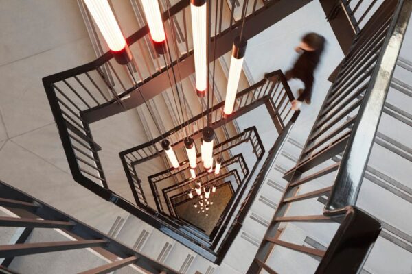 A modern spiral staircase with hanging tube lights and a person walking down.