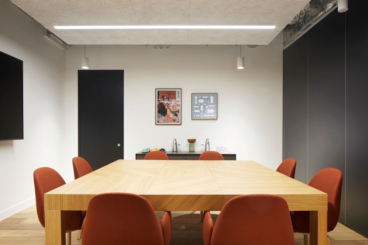 A modern conference room with a large wooden table, orange chairs, artwork on the wall, and minimalist decor.