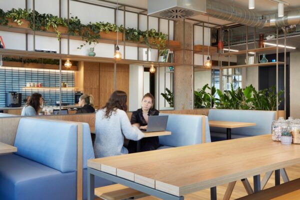 A modern office space featuring two people working at a table with plants and a coffee machine in the background.