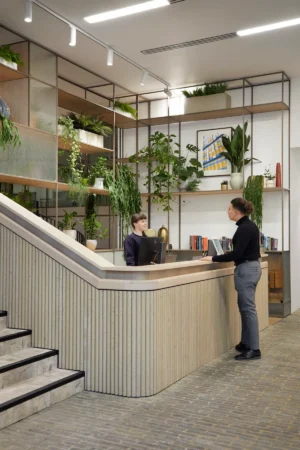 A modern reception area with two people interacting, surrounded by lush indoor plants.
