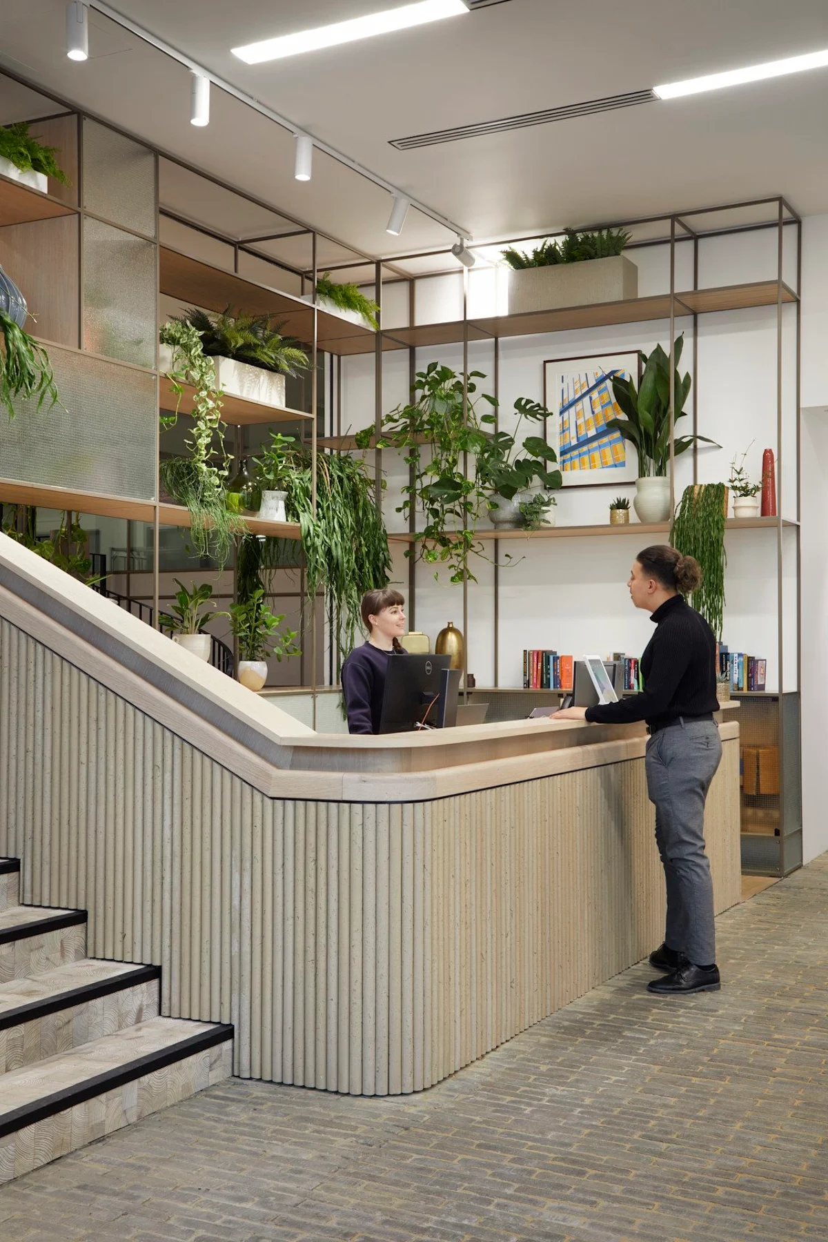 A modern reception area with two people interacting, surrounded by lush indoor plants.