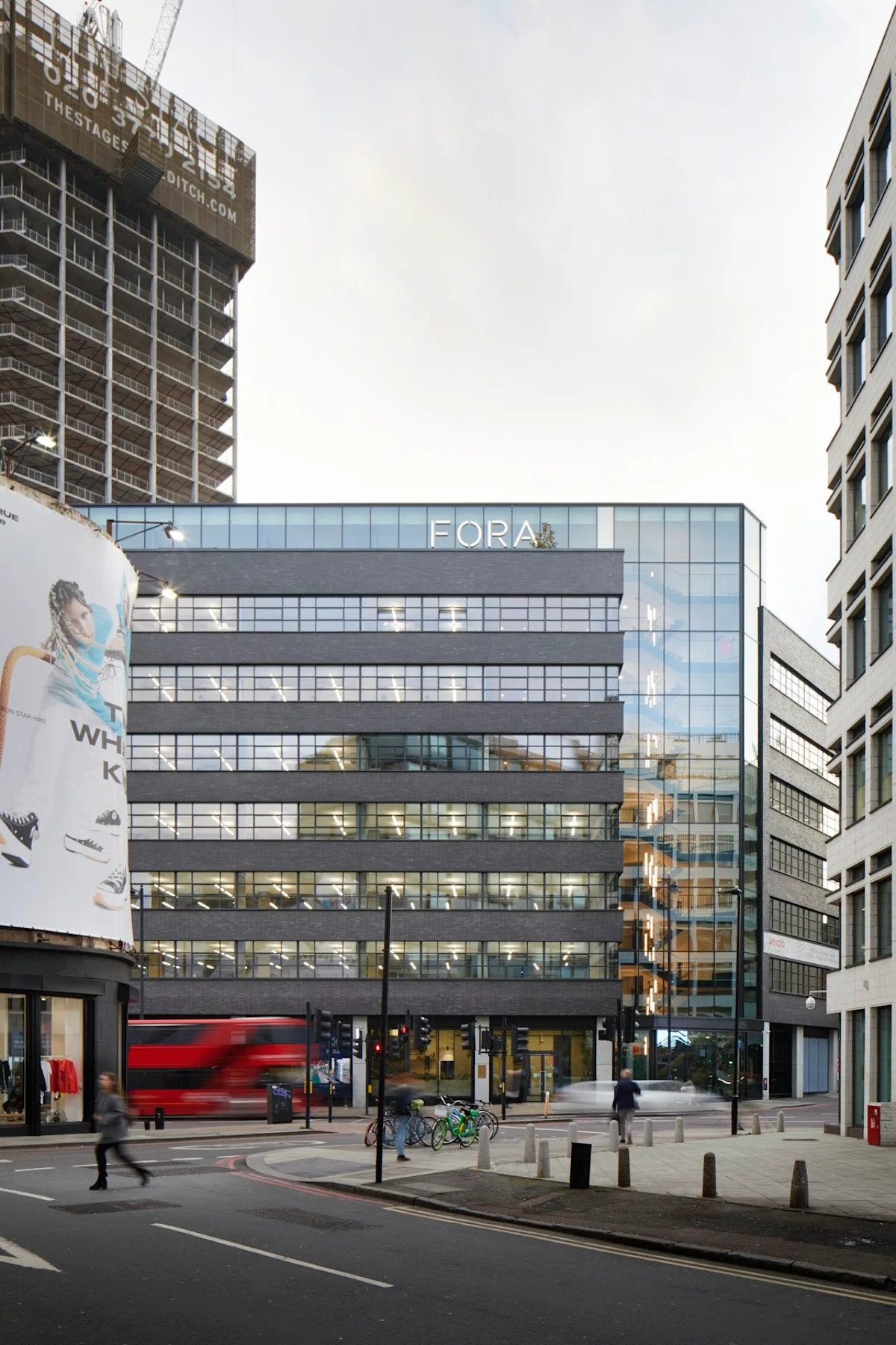 Modern office building on Great Eastern Street in London with a billboard and passing traffic.