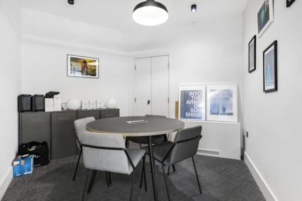 A small meeting room with a round table, four gray chairs, and framed artwork on the walls.