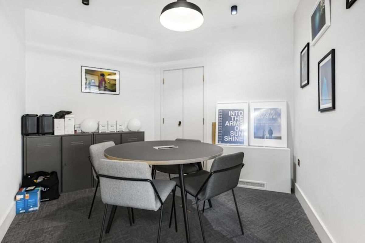 A small meeting room with a round table, four gray chairs, and framed artwork on the walls.